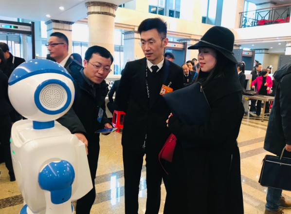 1月13日，政协湖北省十二届二次会议在洪山礼堂开幕。长江云机器人记者“云朵”，连续四年参与两会采访！图为参会委员与“云朵”互动。